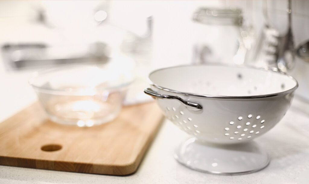 white metal colander with a wooden chopping board and glass bowl at the back