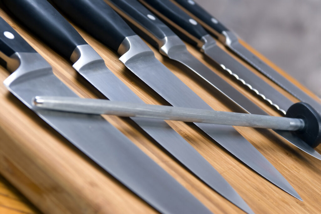 closeup image of a knife set laid out on a wooden chopping board with a sharpening rod across it