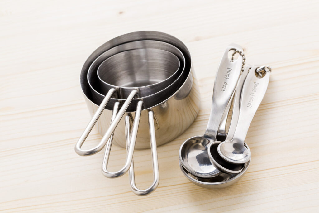 on a light colored wooden surface are stainless steel measuring cups and measuring spoons