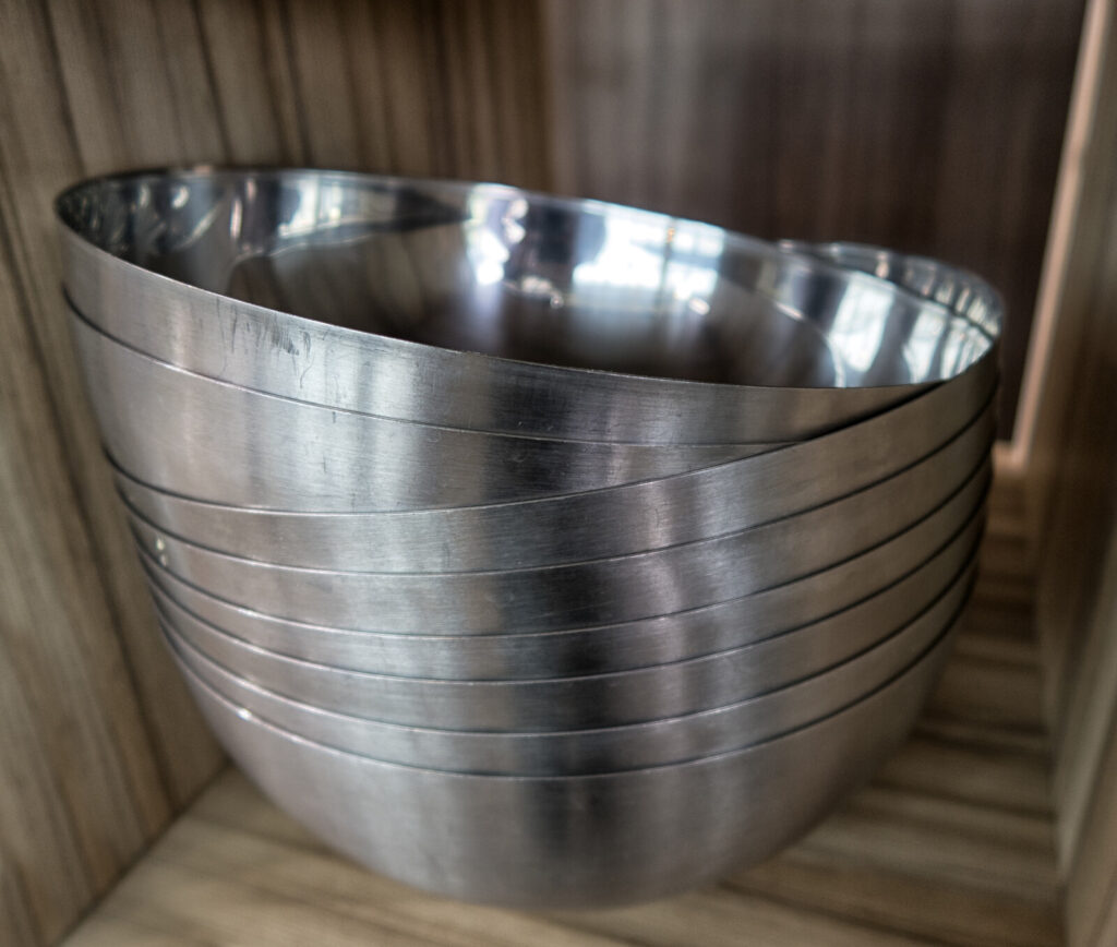 a pile of stainless steel mixing bowls in a wooden cabinet