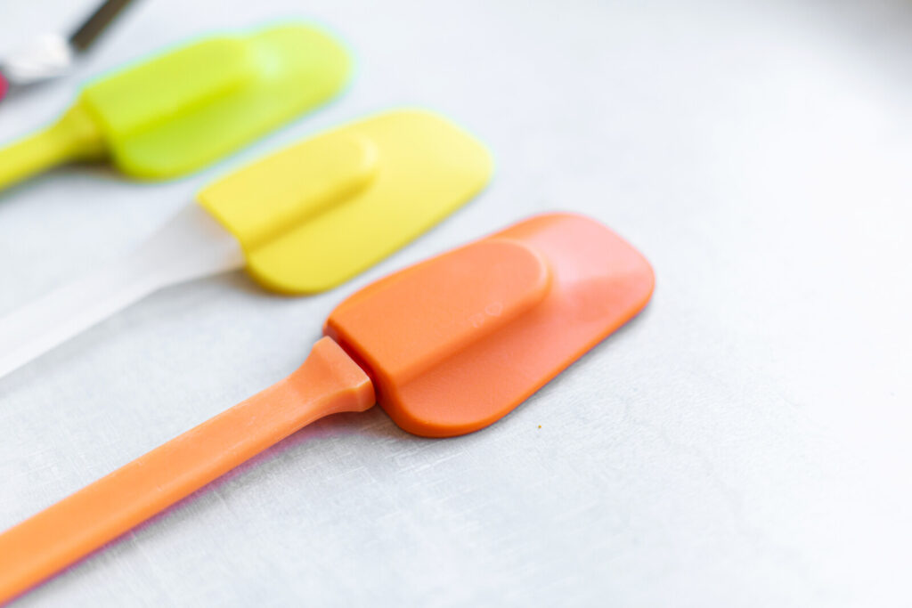 closeup image of a yellow green, yellow, and orange silicon spatulas laid out on a white surface