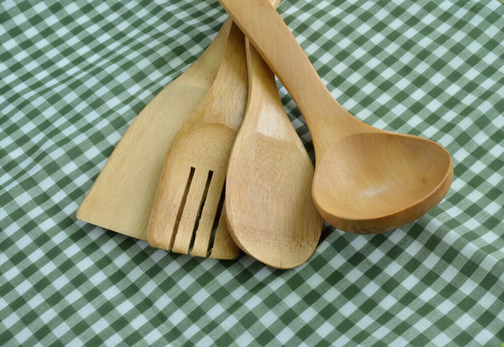 wooden ladles and fish turners laid out on a checkered white and green table cloth