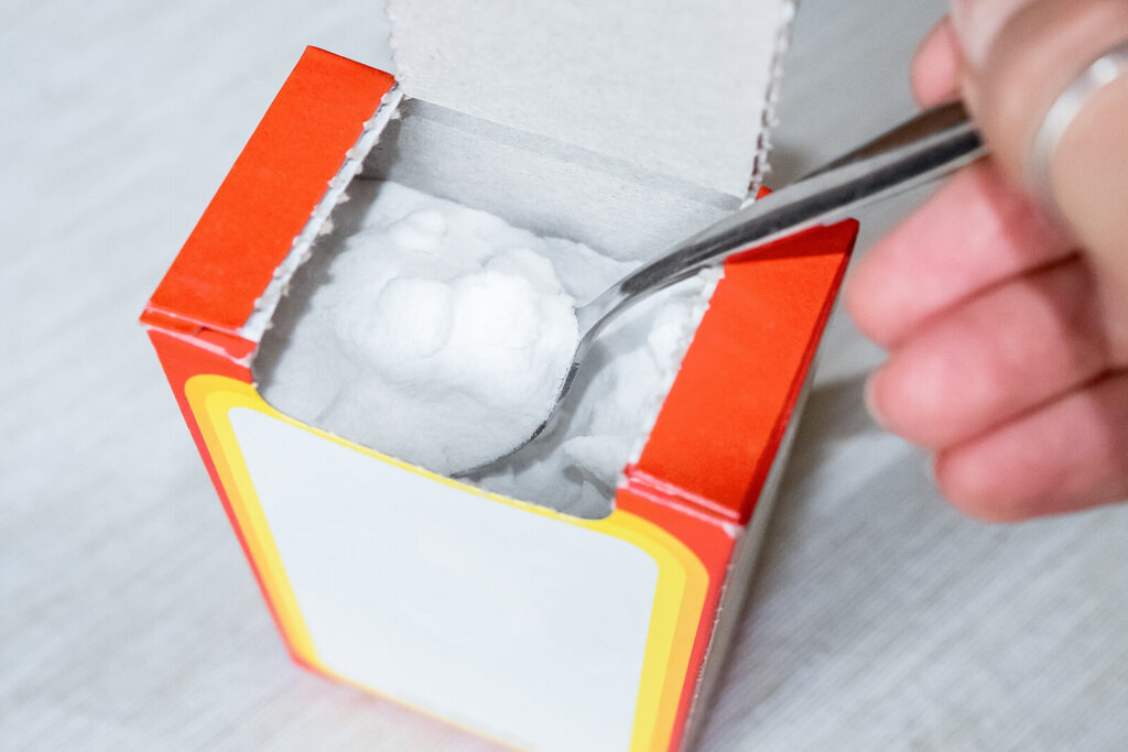 partial image of a hand scooping out baking soda from its carton box