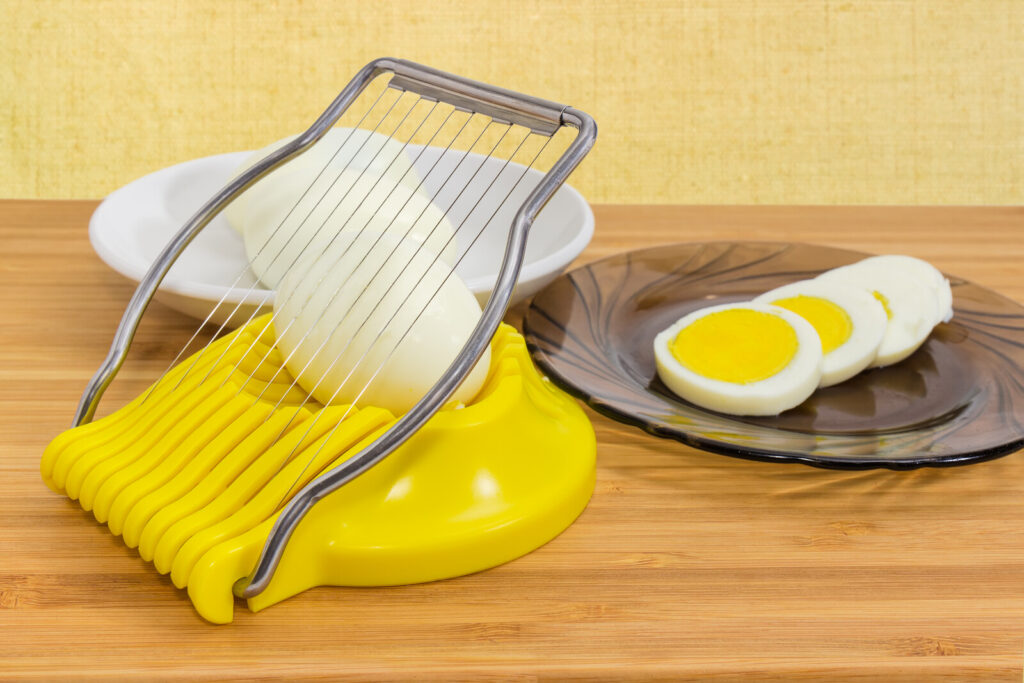 egg slicer on a wooden table with an egg on it and a sliced one on a saucer beside it