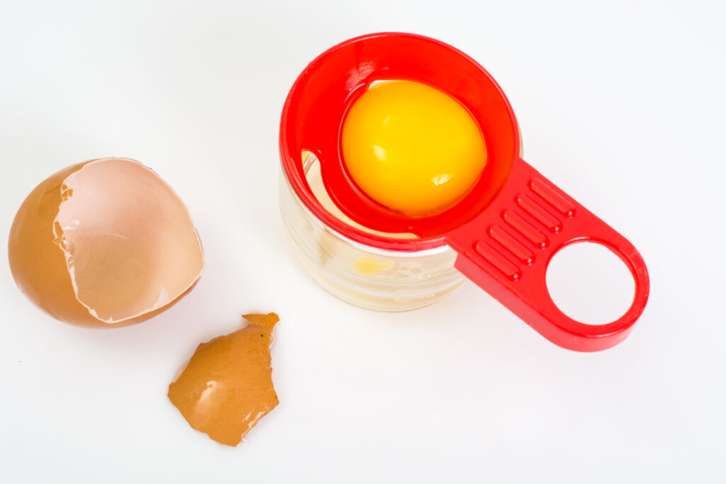 egg yolk separator on a white background with a yolk and brown eggshell beside it