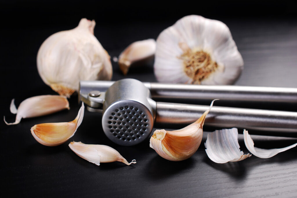 garlic masher with a couple garlic heads and garlic cloves, one of the kitchen tools in the list