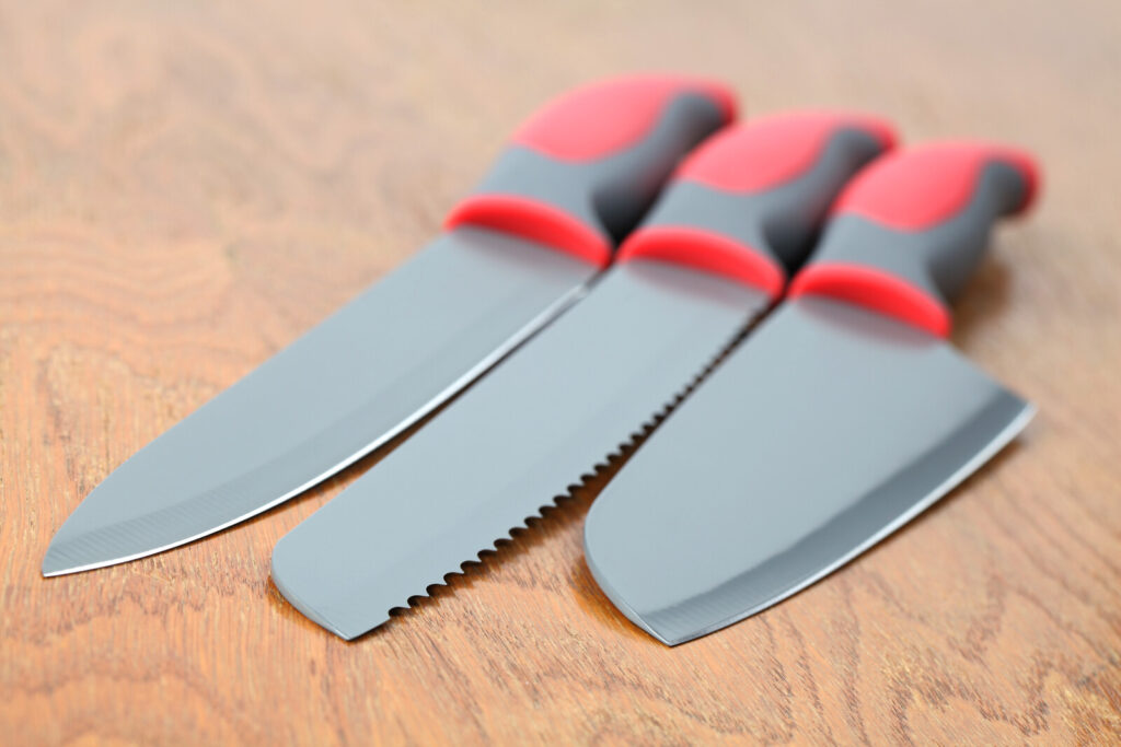 on a wooden surface are three kitchen knives, one of the kitchen tools in the list