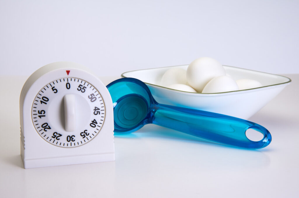 kitchen timer on a kitchen counter with a blue plastic scoop beside it and a bowl of eggs