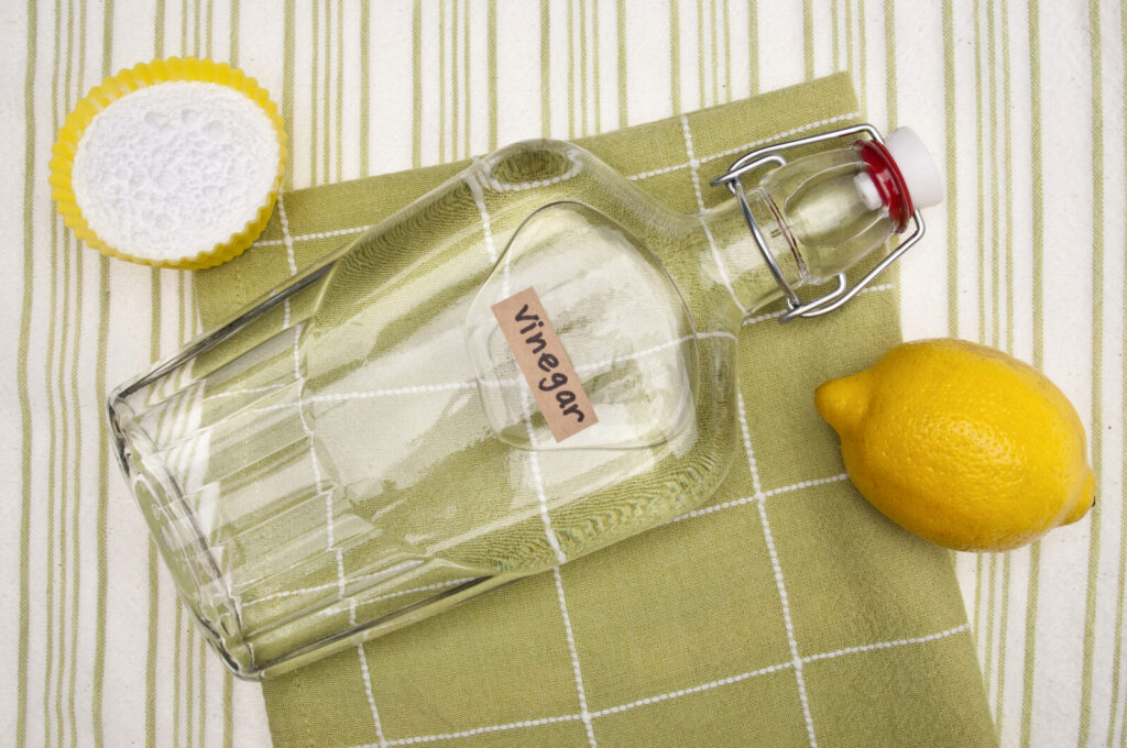 a clear bottle with white vinegar on a green kitchen towel with a lemon and baking soda beside it