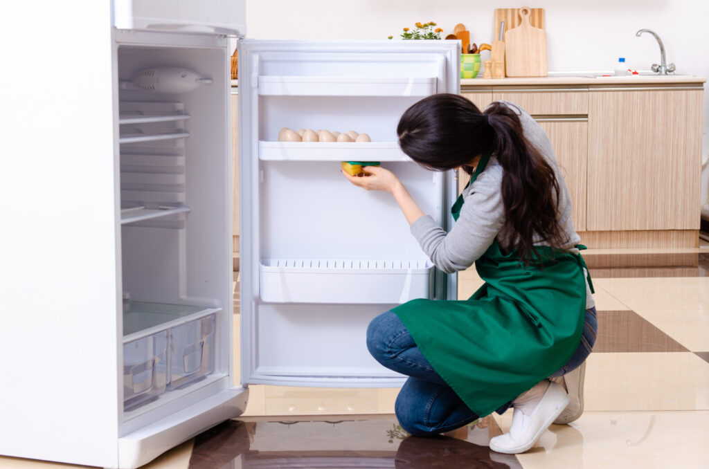 a woman cleaning her fridge, representing the article "MarieKondo-ing Your Fridge: How To Organize Your Refrigerator" by My Kitchendom