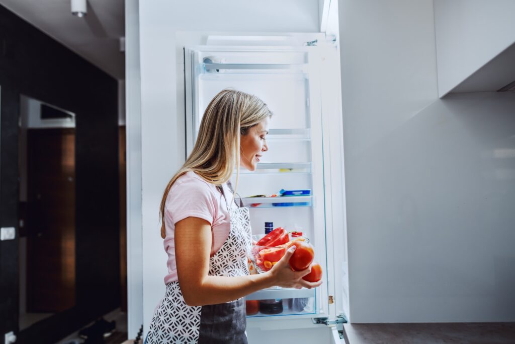 a woman decluttering and organizing fridge, representing the article "The Search for the Best Fridge Organizer: One Tub At a time" by My Kitchendom