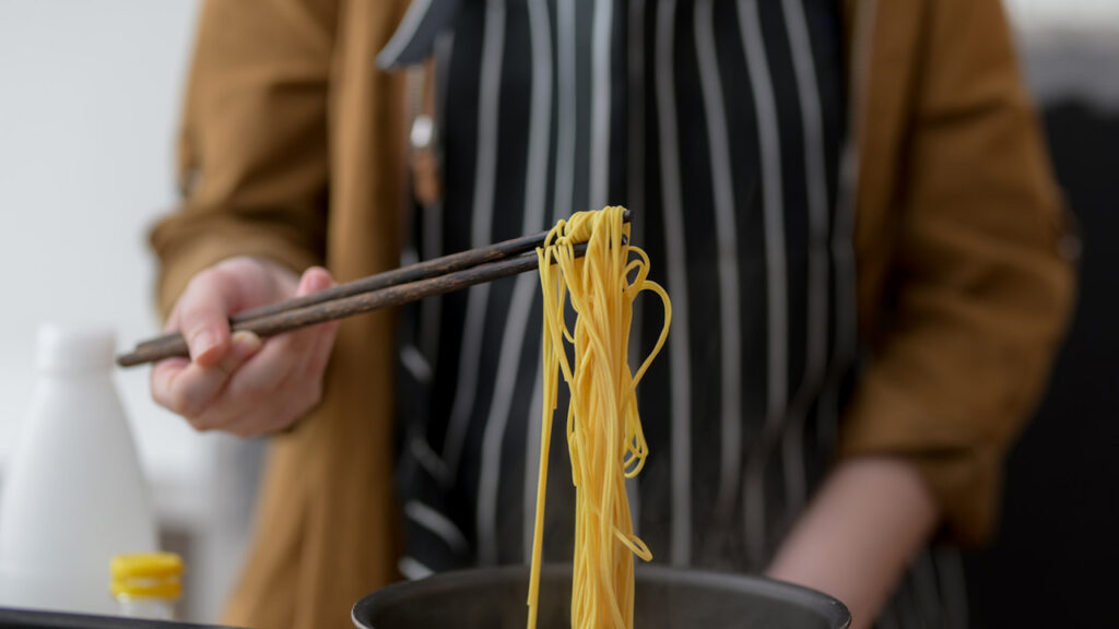 a man holding a freshly cooked pasta with chopsticks, representing the article "But First, How to Cook Pasta" by my kitchendom