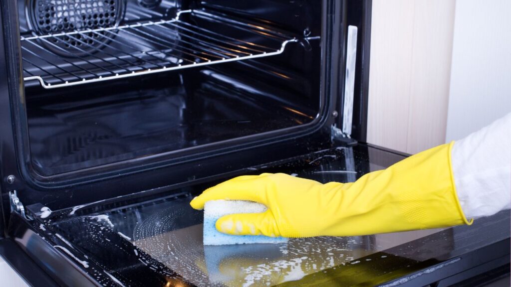 cleaning the oven glass, representing the article "The Best Way To Clean Your Oven" by My Kitchendom